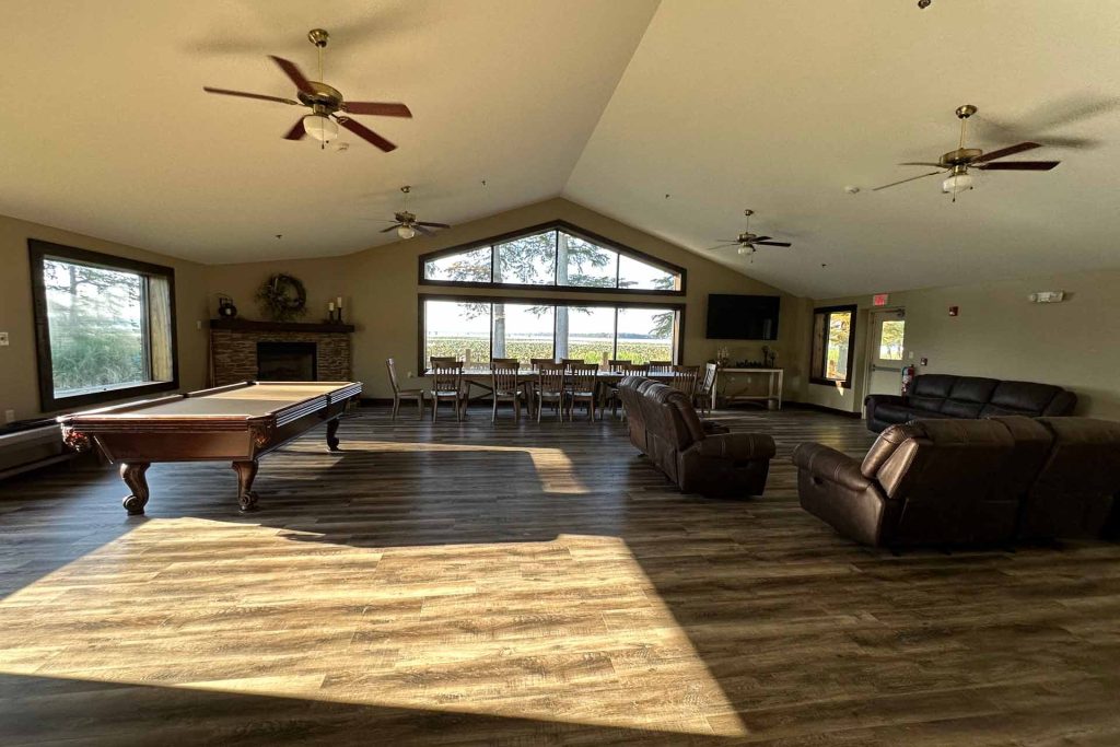 a wide shot of a common room with couches, a fireplace, large windows, and a pool table.